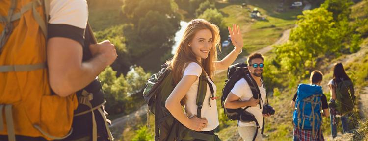 Lächelnde Frau, die in die Kamera schaut und mit der Hand winkt, während sie mit Freunden einen Wanderweg entlangläuft